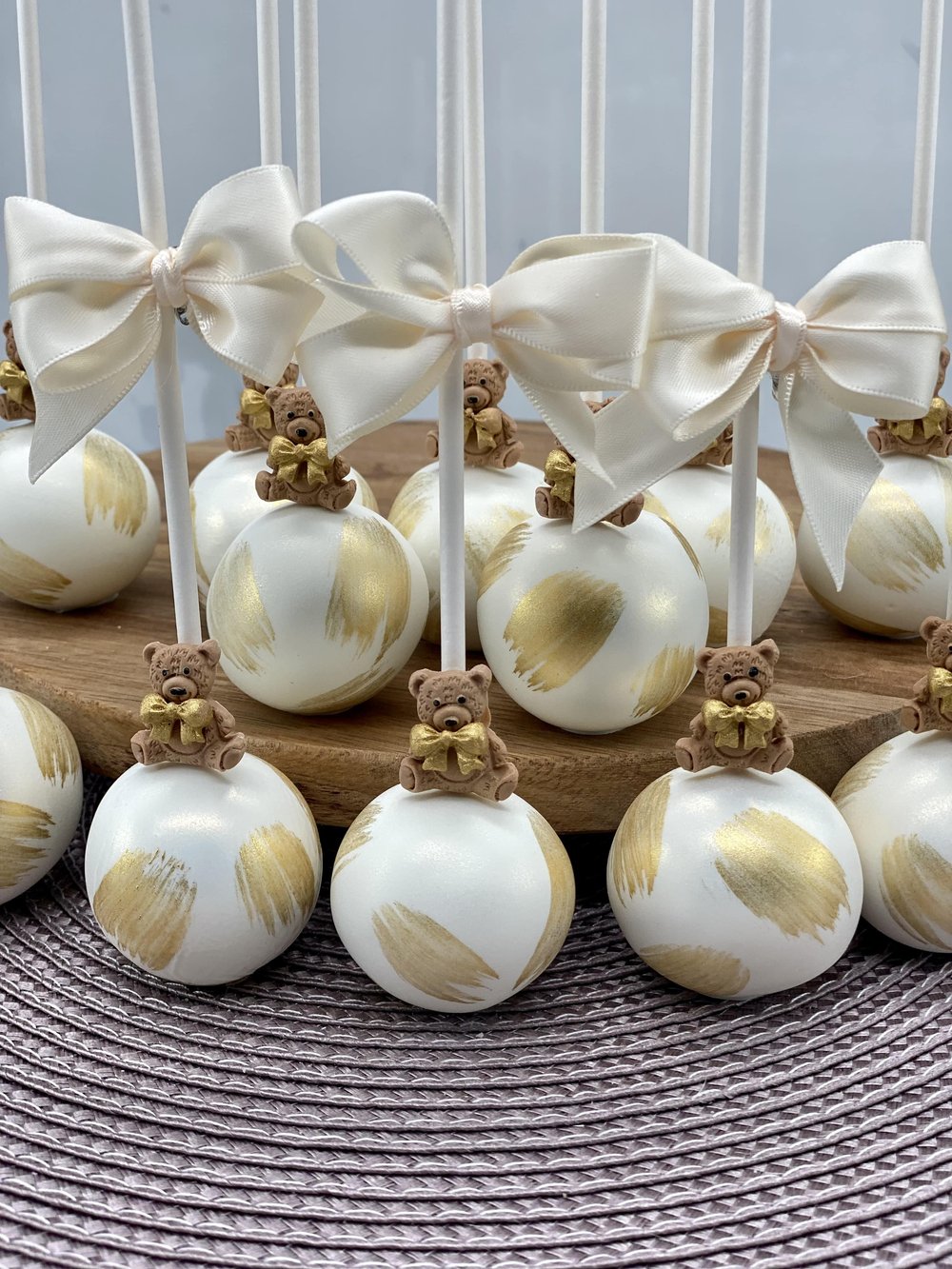 Baby Shower Cakepops with gold accents. Each with a teddybear fondant figure and white satin bow